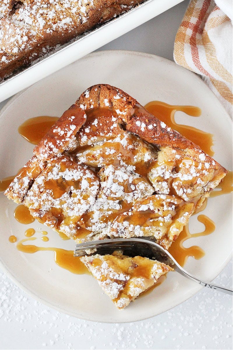 A slice of caramel bread pudding on a plate wtih a fork cutting a bite.