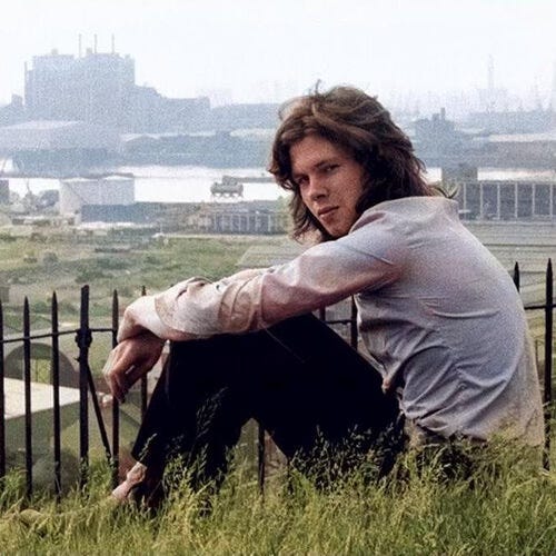 Nick Drake sitting. Behind him a bleak landscape.