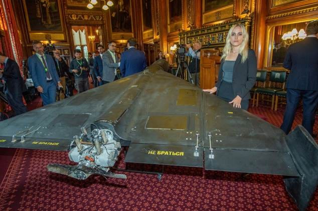 Katie Davis posing next to a Shahed-136 drone with its propeller and engine exposed, displayed indoors.