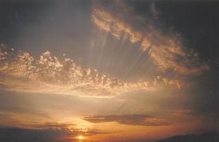 Three images of the sunset over a beach. The final image features sun rays scattered across the clouds