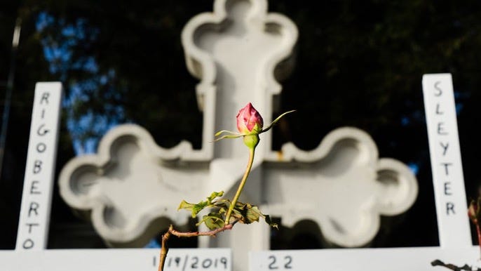 White memorial cross and pink flower plant, with name Rigoberto Sleyter and date 1/19/2019, age 22 to commemorate a victim of gun violence in Oakland, CA