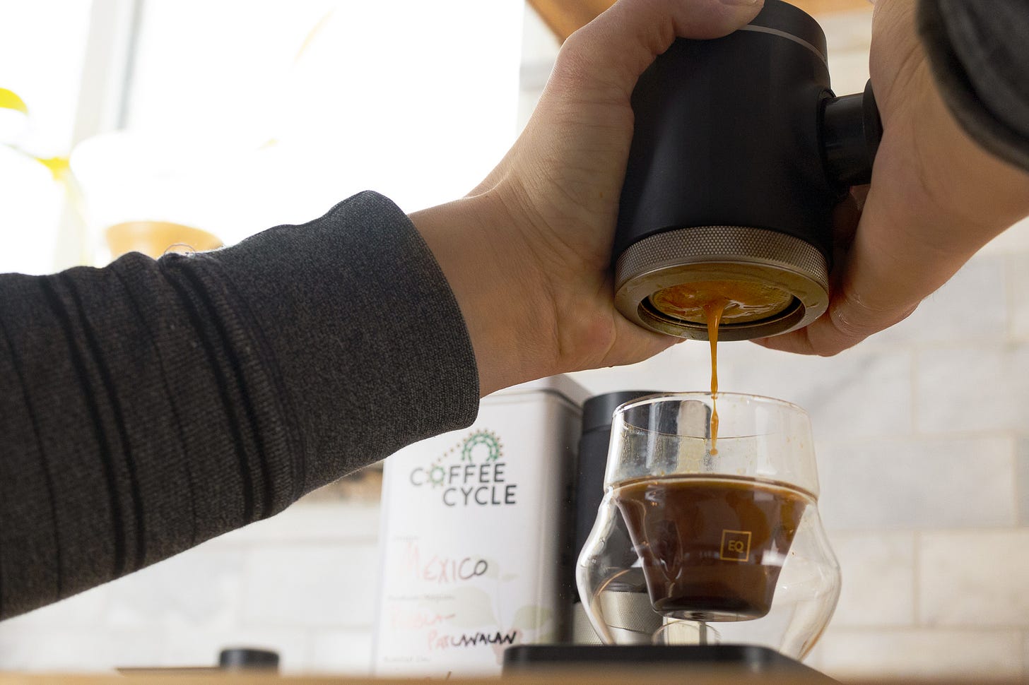 A close-up of coffee pour out of a handheld espresso maker into an espresso shot style cup.