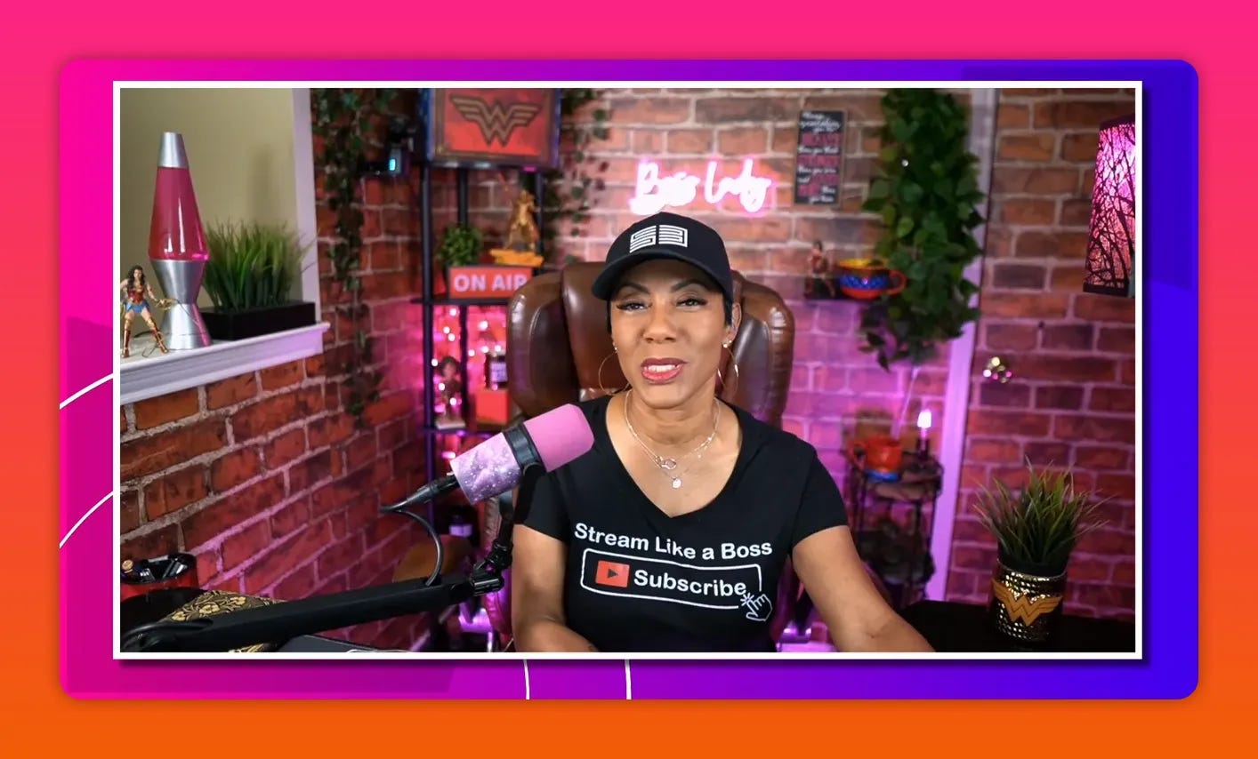 Streamer speaking calmly in a well-lit studio with a pink microphone, plants, and a neon 'Boss Lady' sign behind a brick wall.