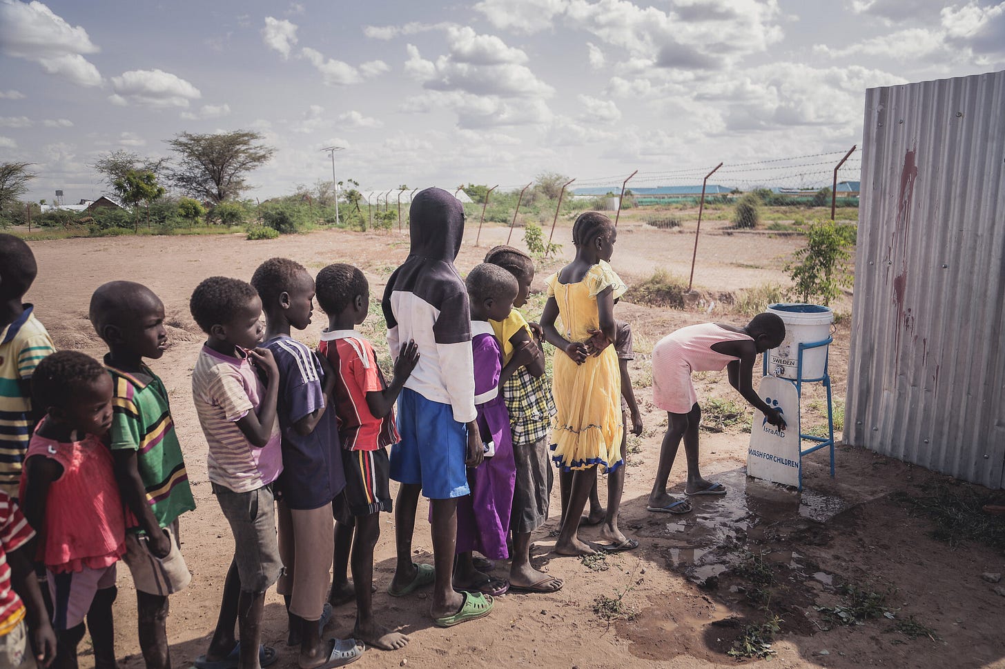 Black children in a line, waiting to get a ration of water in the Kakuma refugee camp. Black children in a line, waiting to get a ration of water in the Kakuma refugee camp.