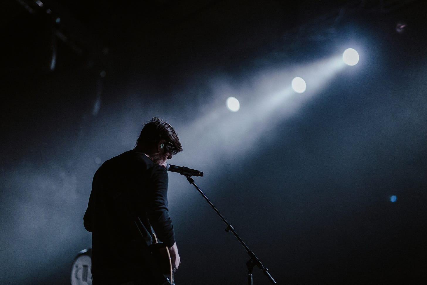 Singer with guitar and microphone looking out over a darkened concert venue