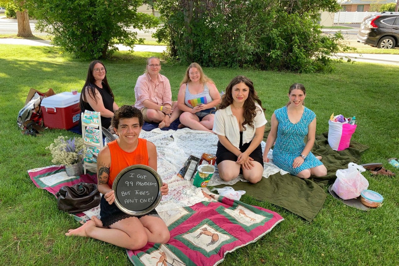 A photo shows Dani Marietti with her friends sitting on the grass set up for a picnic. She is holding a sign that reads, "I got 99 problems, but tubes ain't one." A photo shows Dani Marietti with her friends sitting on the grass set up for a picnic. She is holding a sign that reads, "I got 99 problems, but tubes ain't one."