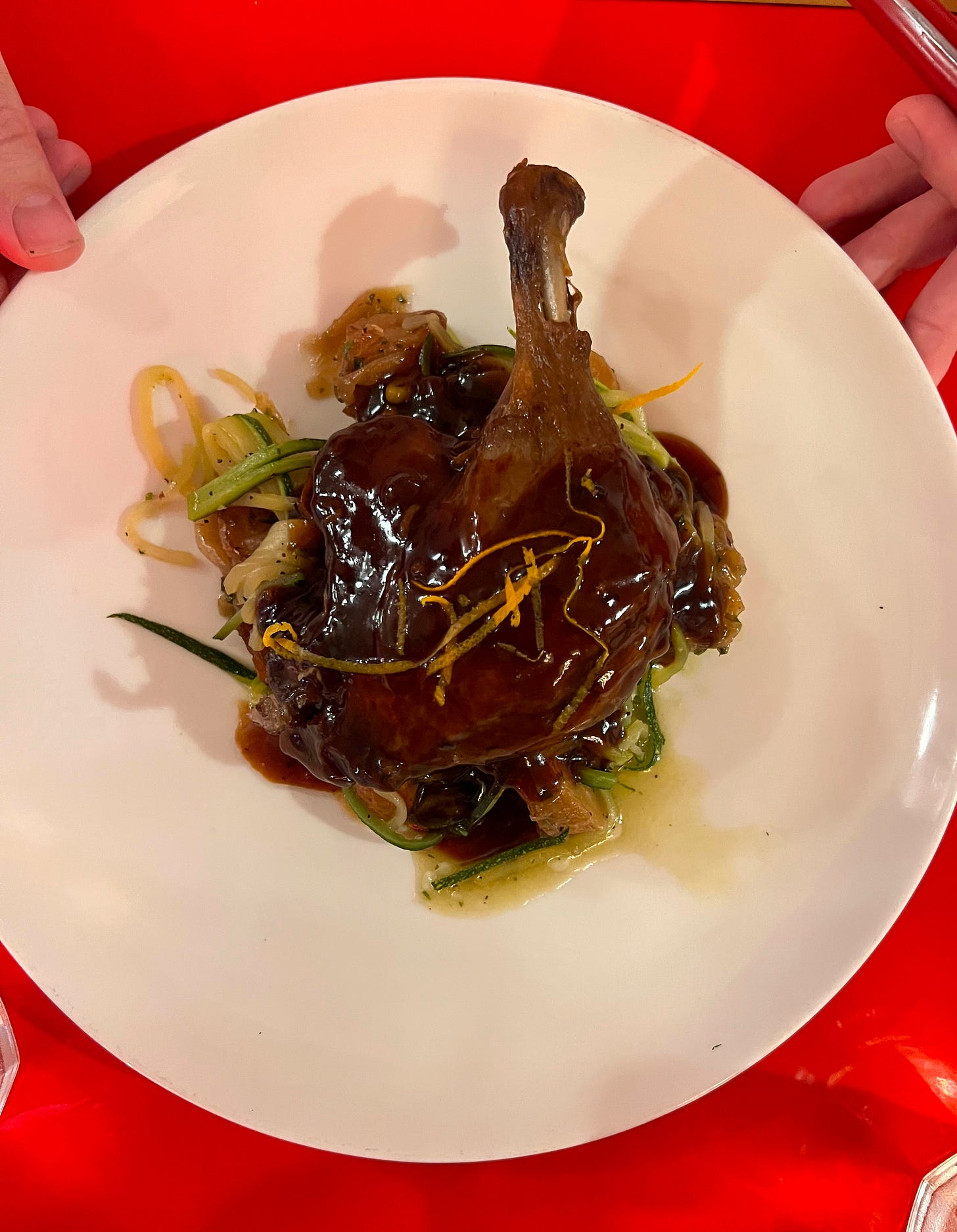 A duck confit leg glazed in dark orange sauce with citrus zest, served over sarladaise potatoes and green vegetables at Bouillon by Moulin.