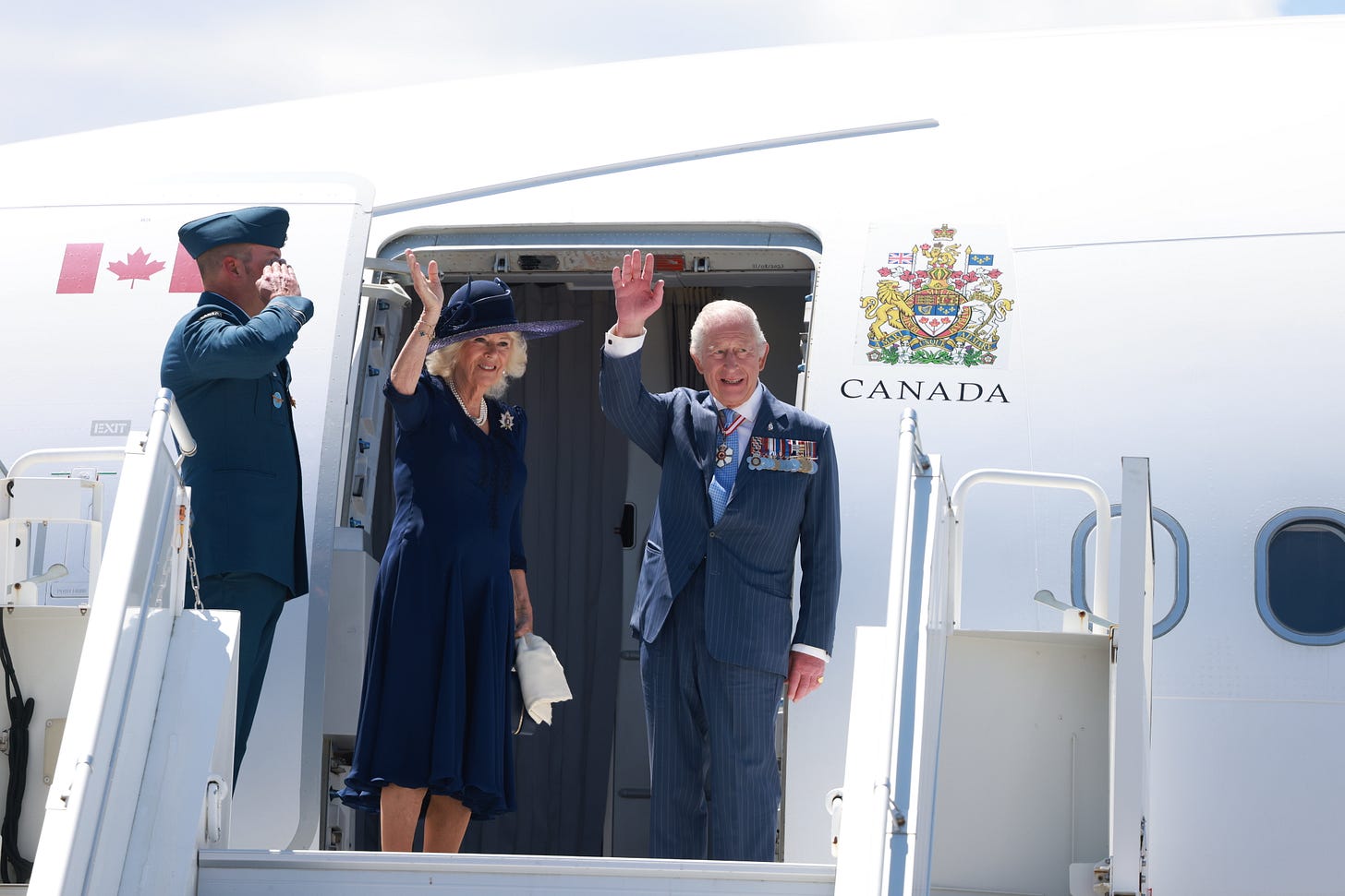 Queen Camilla and King Charles waving from a plane