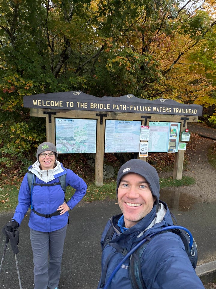 a man and woman at trailhead sign at Falling Waters in NH and tree roots growing over a boulder