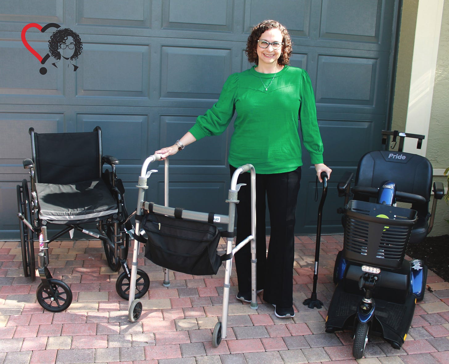 The writer is standing amid 4 medical devices: from left to right are a wheelchair, walker, cane, and mobility scooter.