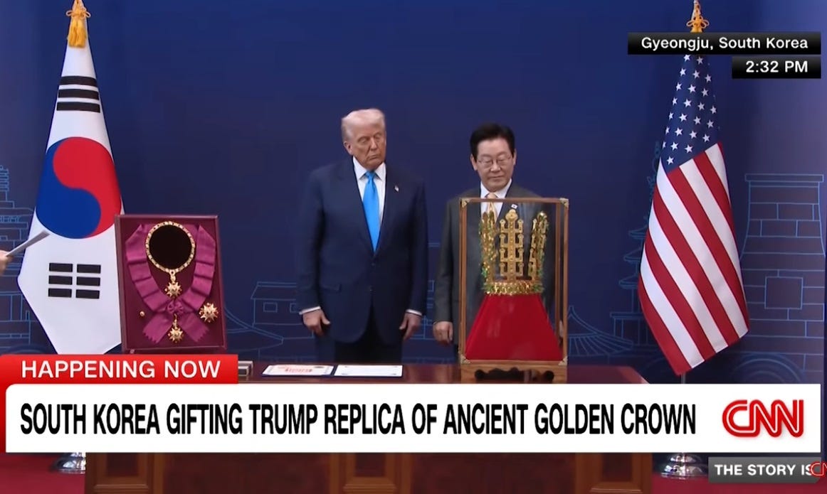 CNN screenshot showing Donald Trump standing solemnly next to South Korean President Lee Jae Myung as they both look at a replica of a big golden crown in a glass display case. Also on the table before them is a framed medal and ribbon for the ''Grand Order of Mugunghwa,' South Korea's 'highest civilian decoration,' given to each elected ROK president and sometimes to visiting foreign leaders. The scene is flanked by US and Republic of Korea flags. CNN screenshot showing Donald Trump standing solemnly next to South Korean President Lee Jae Myung as they both look at a replica of a big golden crown in a glass display case. Also on the table before them is a framed medal and ribbon for the ''Grand Order of Mugunghwa,' South Korea's 'highest civilian decoration,' given to each elected ROK president and sometimes to visiting foreign leaders. The scene is flanked by US and Republic of Korea flags.