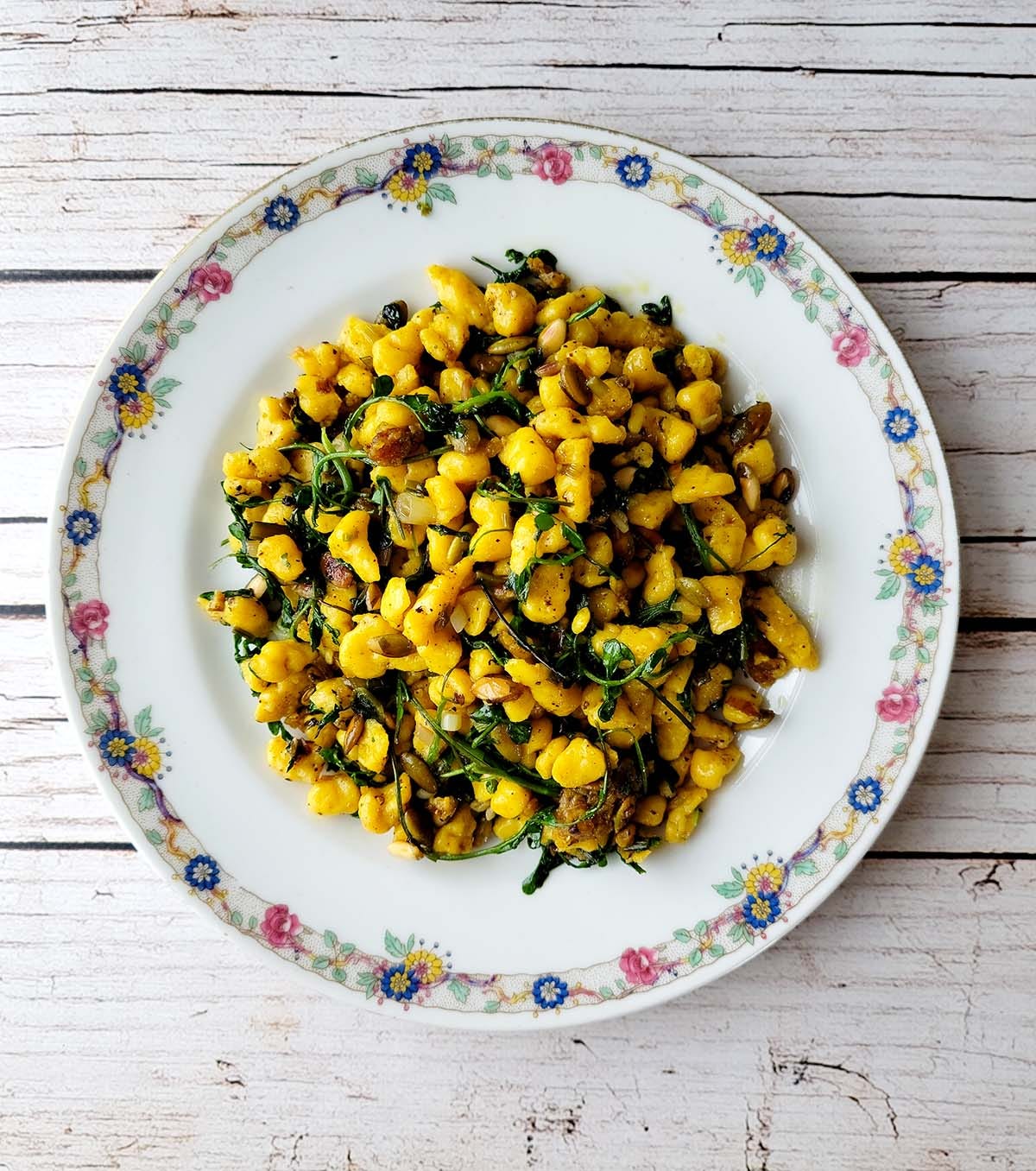 A plate of squash spaetzle with greens on a wooden table. 