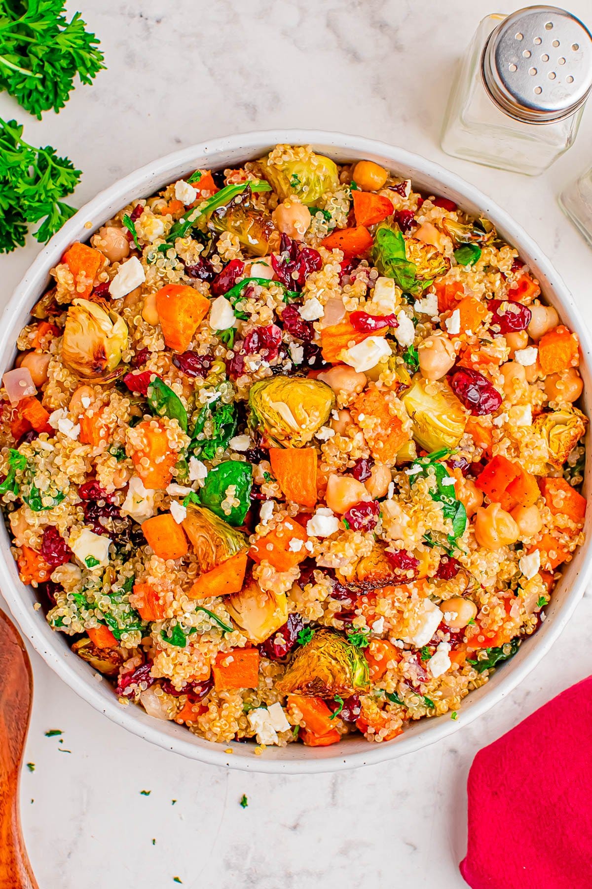 A bowl of quinoa salad with roasted sweet potatoes, Brussels sprouts, chickpeas, dried cranberries, feta cheese, and fresh herbs on a marble surface. A bowl of quinoa salad with roasted sweet potatoes, Brussels sprouts, chickpeas, dried cranberries, feta cheese, and fresh herbs on a marble surface.