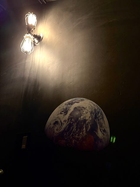 A selfie of the author in an antique mirror, an mural of the Earth, a St. Francis statue under palm trees.