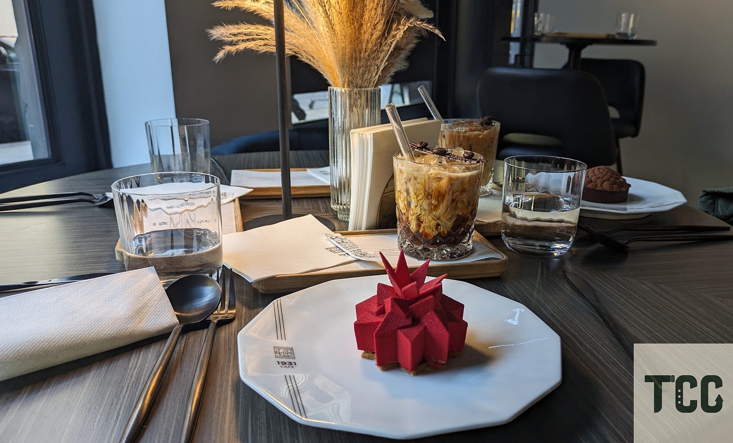 Two pastries on plates, one shaped like a red star (Étoile de Cassis) and another green dome-shaped dessert (Ellipse de Sapin).