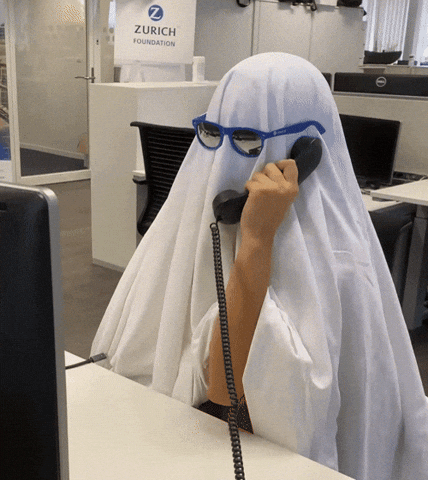 Video gif. In an office a person wears a white sheet over their body and blue sunglasses. They hold up an office phone and nod absentmindedly. Video gif. In an office a person wears a white sheet over their body and blue sunglasses. They hold up an office phone and nod absentmindedly.