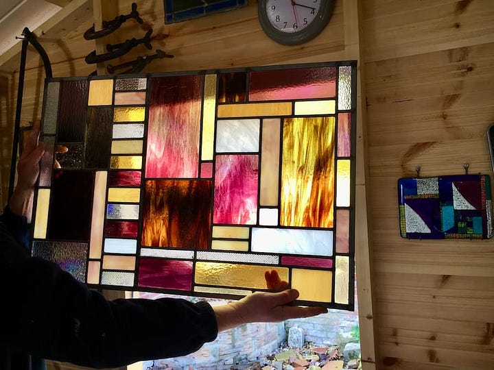 Stained glass panel work in progress, made up of multiple rectangular and square panels of different colours and textures. The colours include brown, yellow, orange, maroon and clear glass.