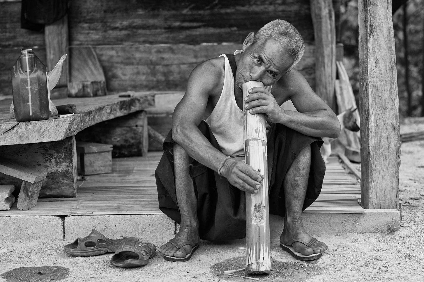 A person sitting on a porch playing a bamboo instrument

Description automatically generated