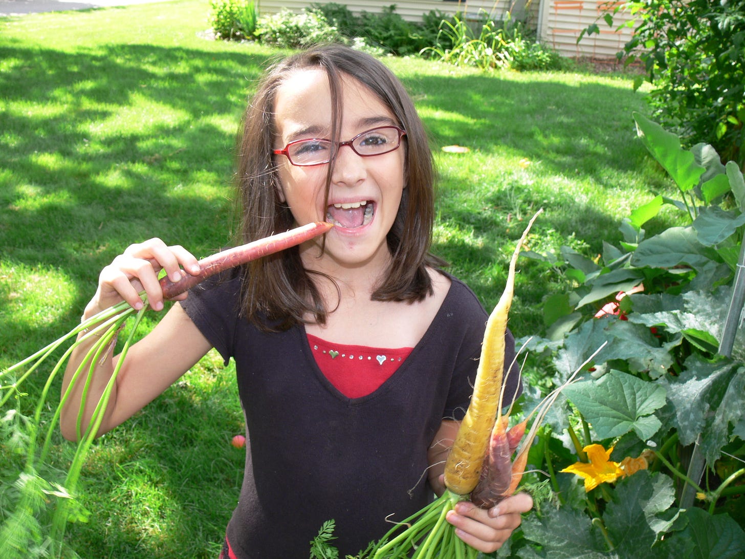 a girl eating carrots next to a garden