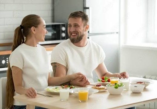 Happy young couple holding hands having breakfast cooked at home sitting at kitchen dining table, married man and woman start eating right well healthy food, enjoying delicious homemade meal together Stock Photo |