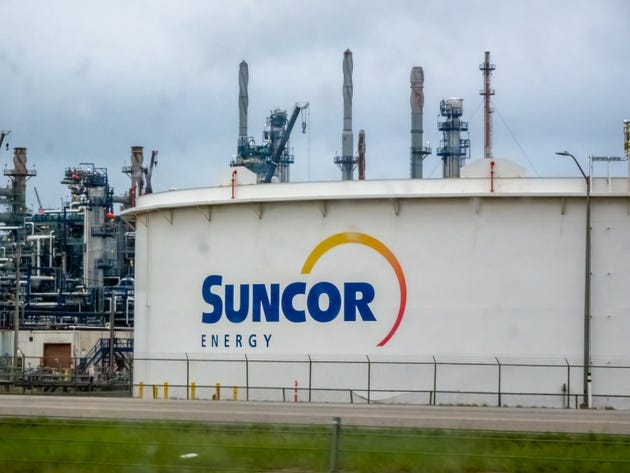The Suncor Energy logo prominently displayed on a large storage tank, set against the backdrop of an industrial refinery complex. The Suncor Energy logo prominently displayed on a large storage tank, set against the backdrop of an industrial refinery complex.