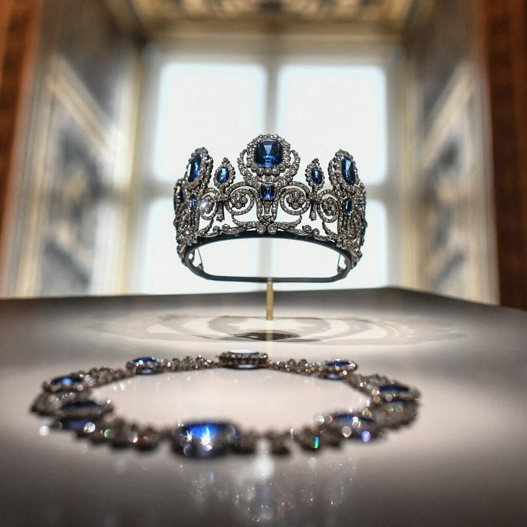 A crown, necklace and earrings decorated with large blue stones and diamonds.