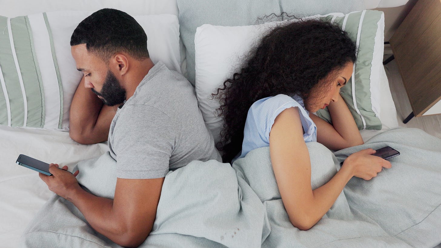Couple scrolling and facing away from each other while lying in bed