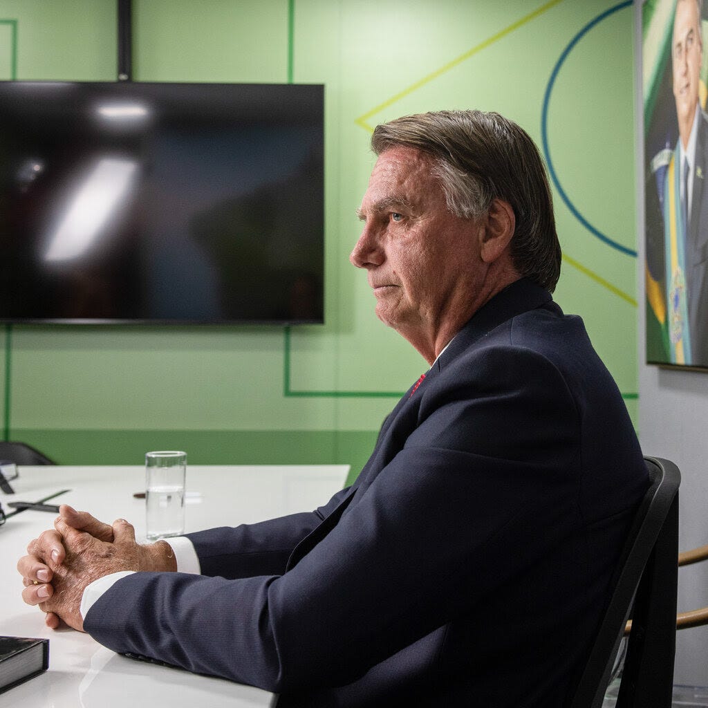 Jair Bolsonaro, the former Brazilian president, wearing a dark suit and sitting at a table.
