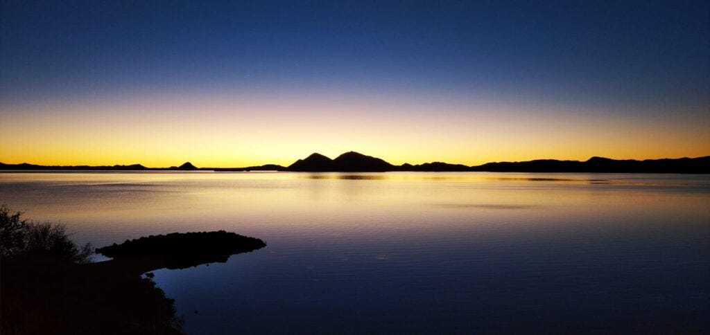Serene lake sunset with mountain silhouettes reflecting golden light on calm water Serene lake sunset with mountain silhouettes reflecting golden light on calm water