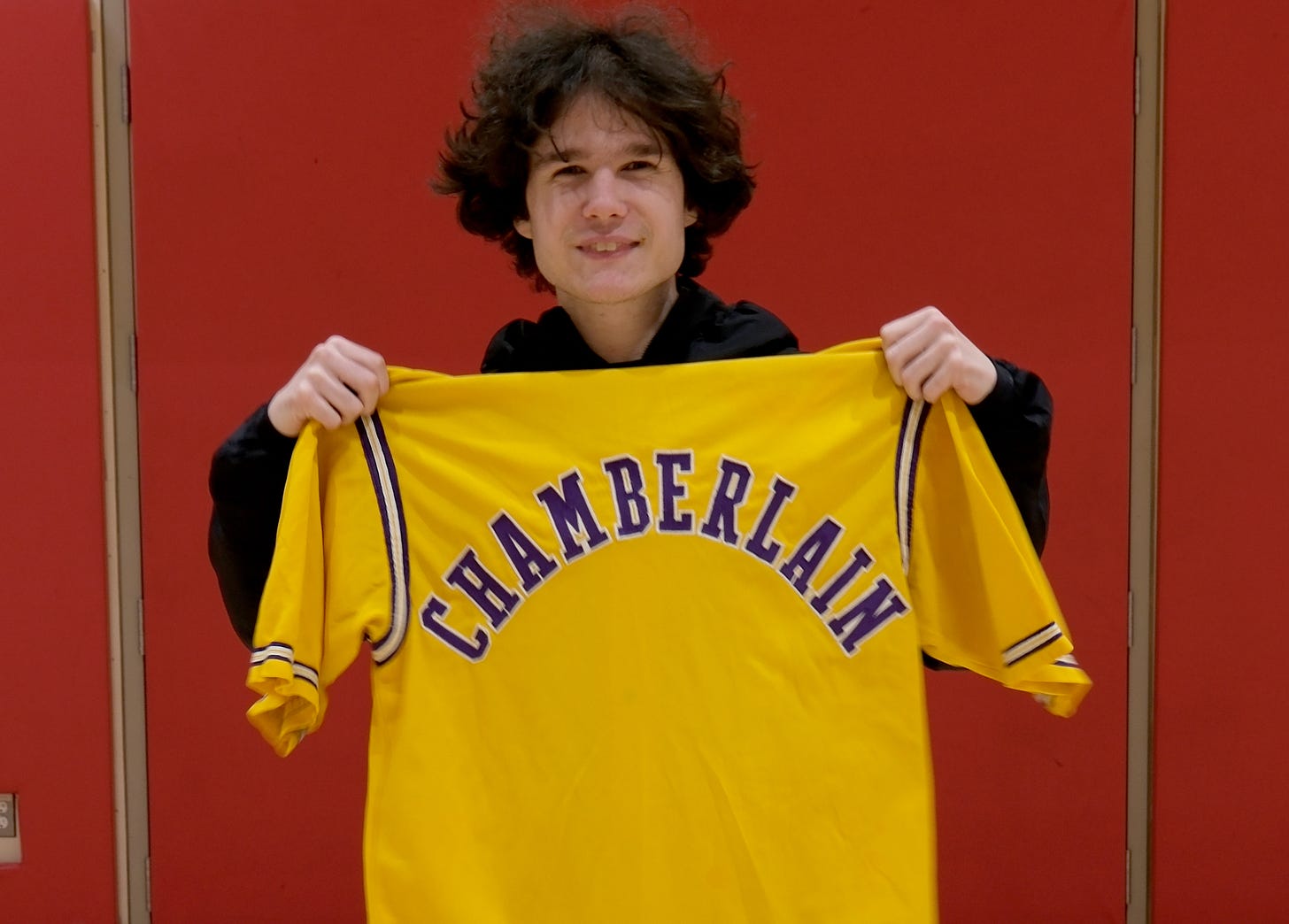 In this provided photo taken in January 2026 at the Multnomah Athletic Club in Portland, Quinn Brown poses with a warm-up jacket worn by basketball legend Wilt Chamberlain during the 1972 NBA Finals. The jacket, which Brown found and bought for $3 at the Goodwill store in Hillsboro, is expected to fetch as much as $250,000 at auction.