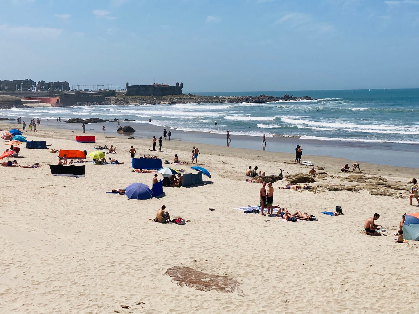 Beach with people on it and a European fort in the background.