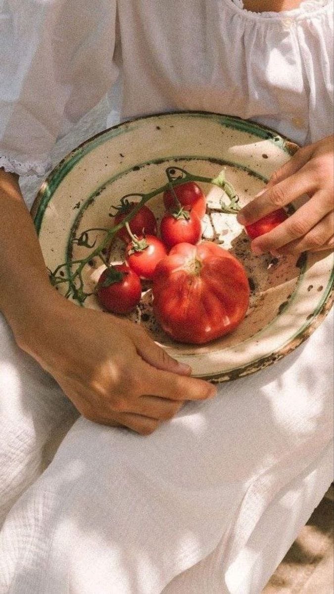 This may contain: a woman is holding a plate with tomatoes on it and she has her hands in the bowl