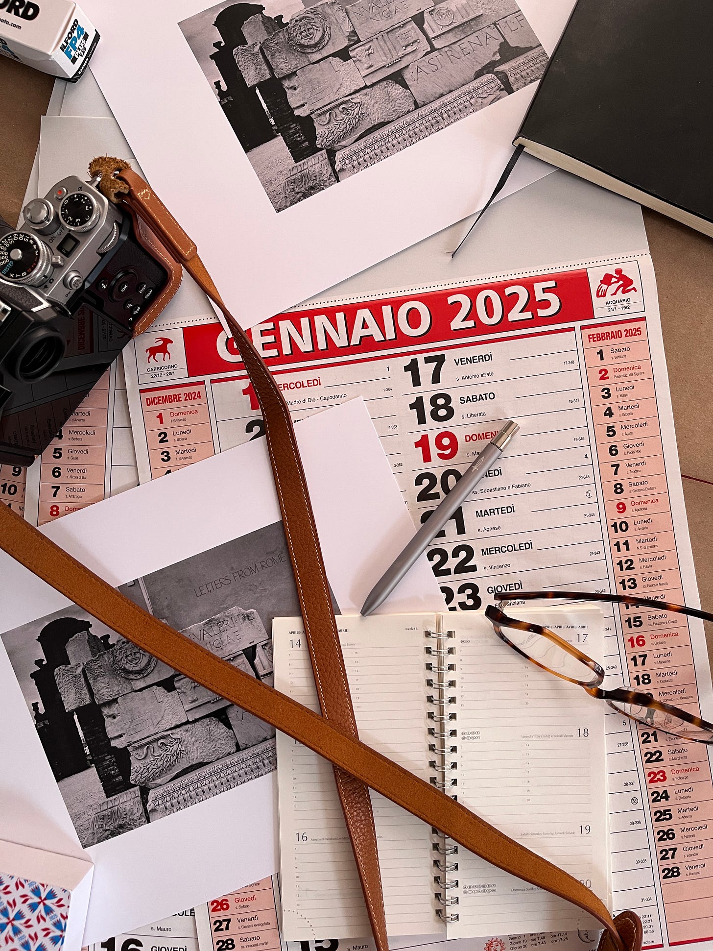 Desk setup featuring an Italian calendar for January 2025, a notebook, a vintage camera, and personal accessories. Photo by Michelle Ciani Desk setup featuring an Italian calendar for January 2025, a notebook, a vintage camera, and personal accessories. Photo by Michelle Ciani