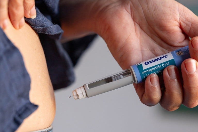 Close up view of a person holding an Ozempic needle injection pen close to their stomach. Close up view of a person holding an Ozempic needle injection pen close to their stomach.