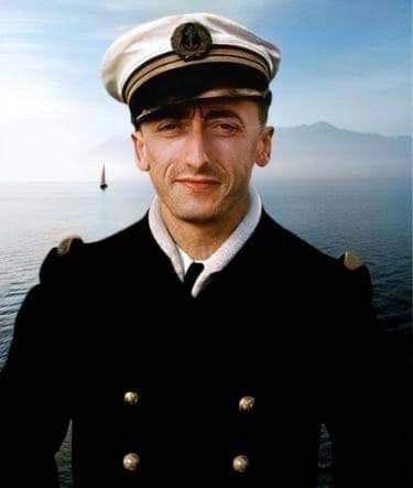 This may contain: a man in a sailor's uniform standing on the deck of a boat looking at the camera