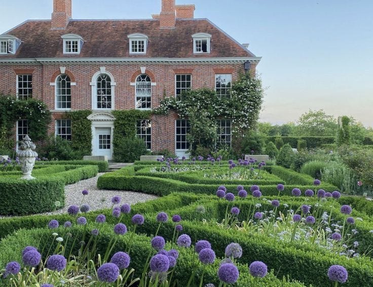 This may contain: a large brick house surrounded by lush green hedges and purple flowers in the foreground This may contain: a large brick house surrounded by lush green hedges and purple flowers in the foreground