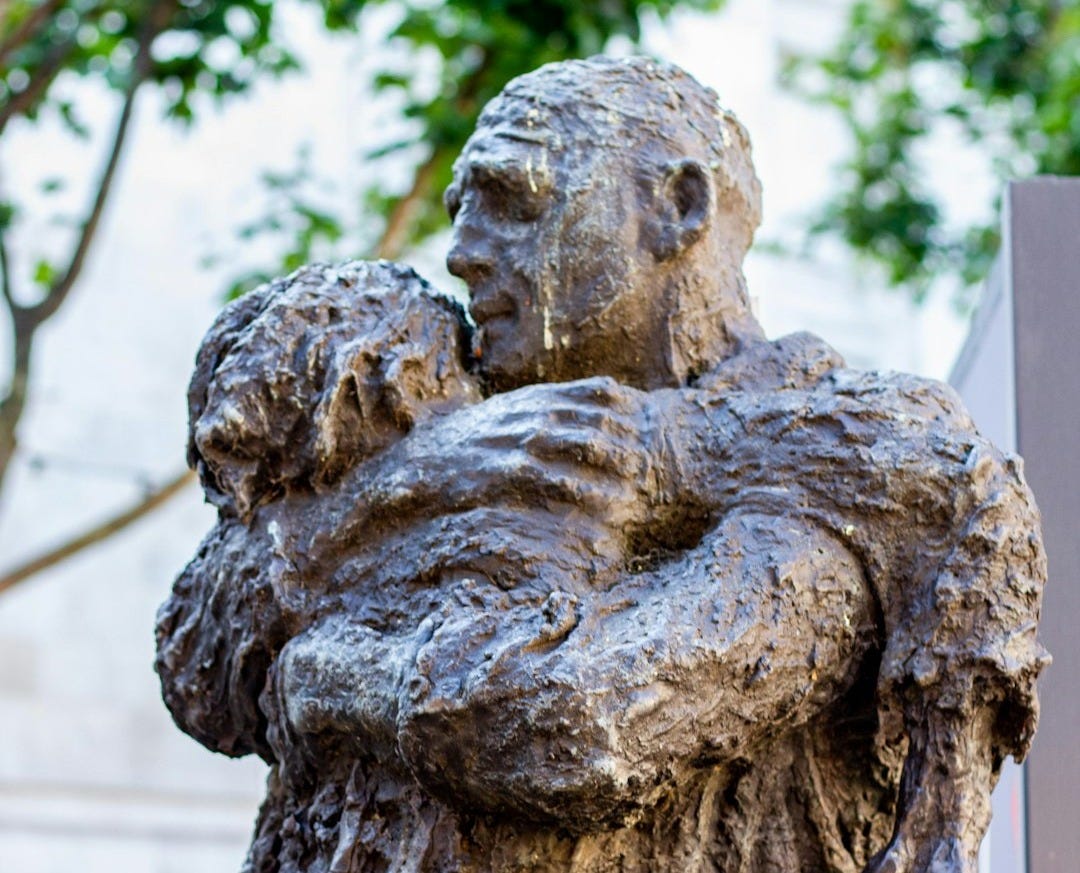 A bronze sculpture depicts a man hugging a child. A bronze sculpture depicts a man hugging a child.