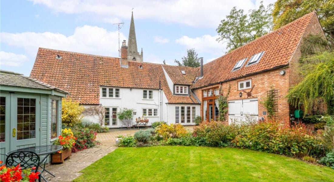 A white cottage with a lawn in front of it, a green summerhouse to the left, and a spire above it