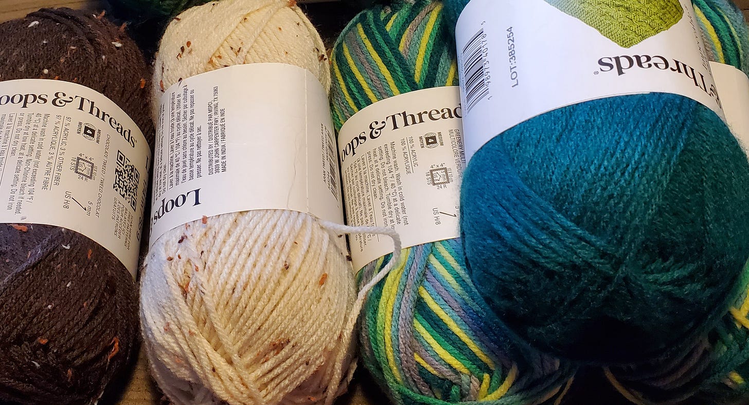 Five skeins of yarn: brown with spots, cream with spots, two green variegated, and one emerald green.