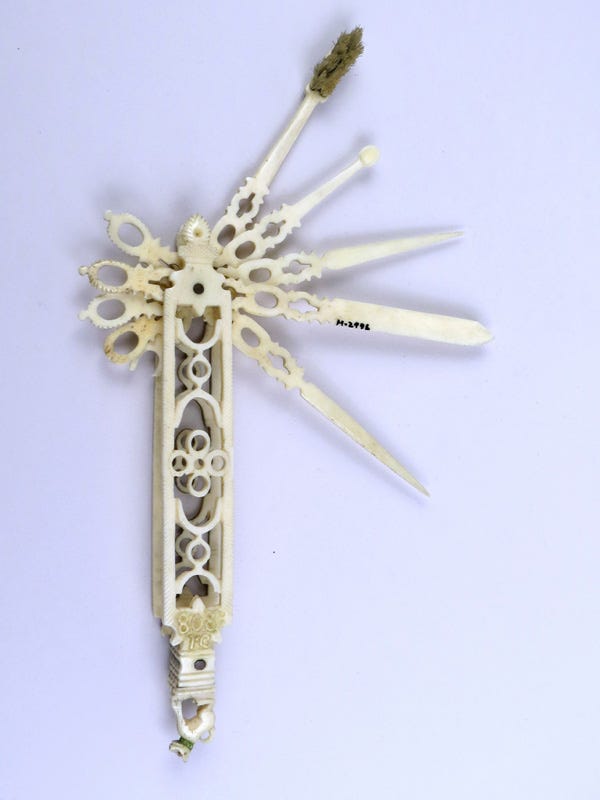 A personal hygiene device opened to show various implements, including a toothbrush. One end of the device is decorated with a tiny carving of a dog with a green collar.