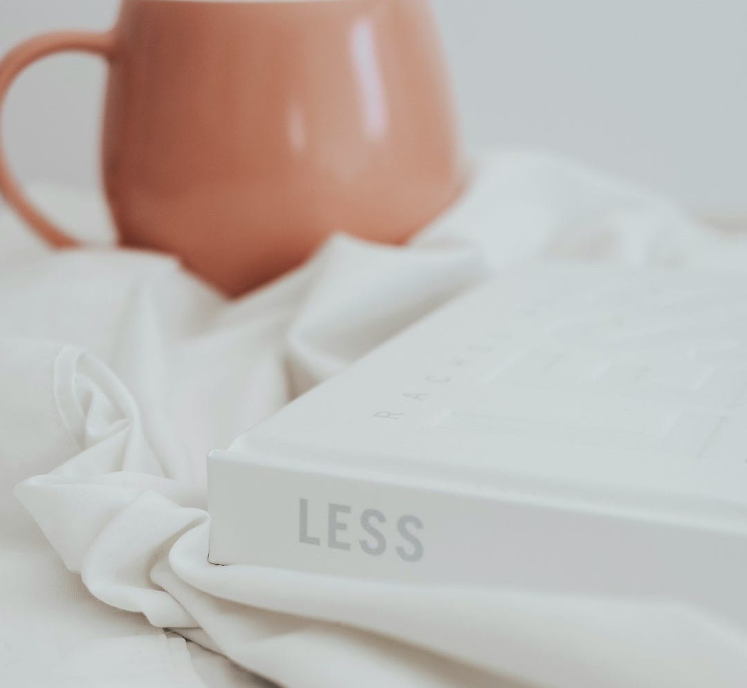 a coffee mug sitting on top of a bed next to a book