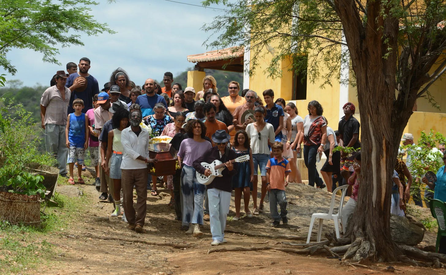 Film still from Bacurau. A group of villagers walk together, carrying food and instruments.