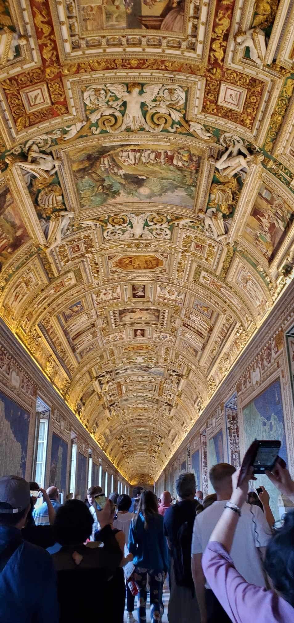 crowds line the hallway under the gold glided ceilings at the Vatican Museum.