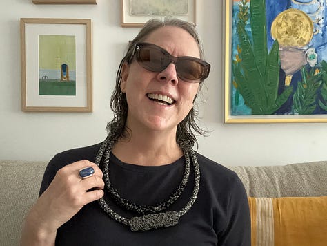 a woman wearing different necklaces, jewelry hanging on the wall and designers clothes hanging