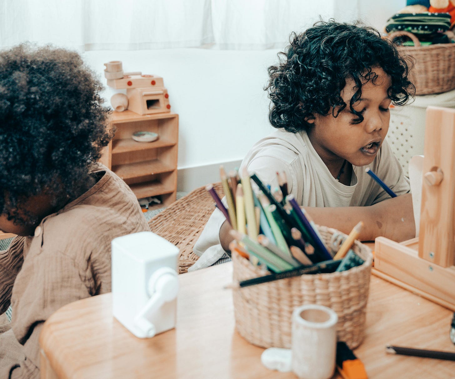 Black kid drawing near crop unrecognizable sister sitting in apartment