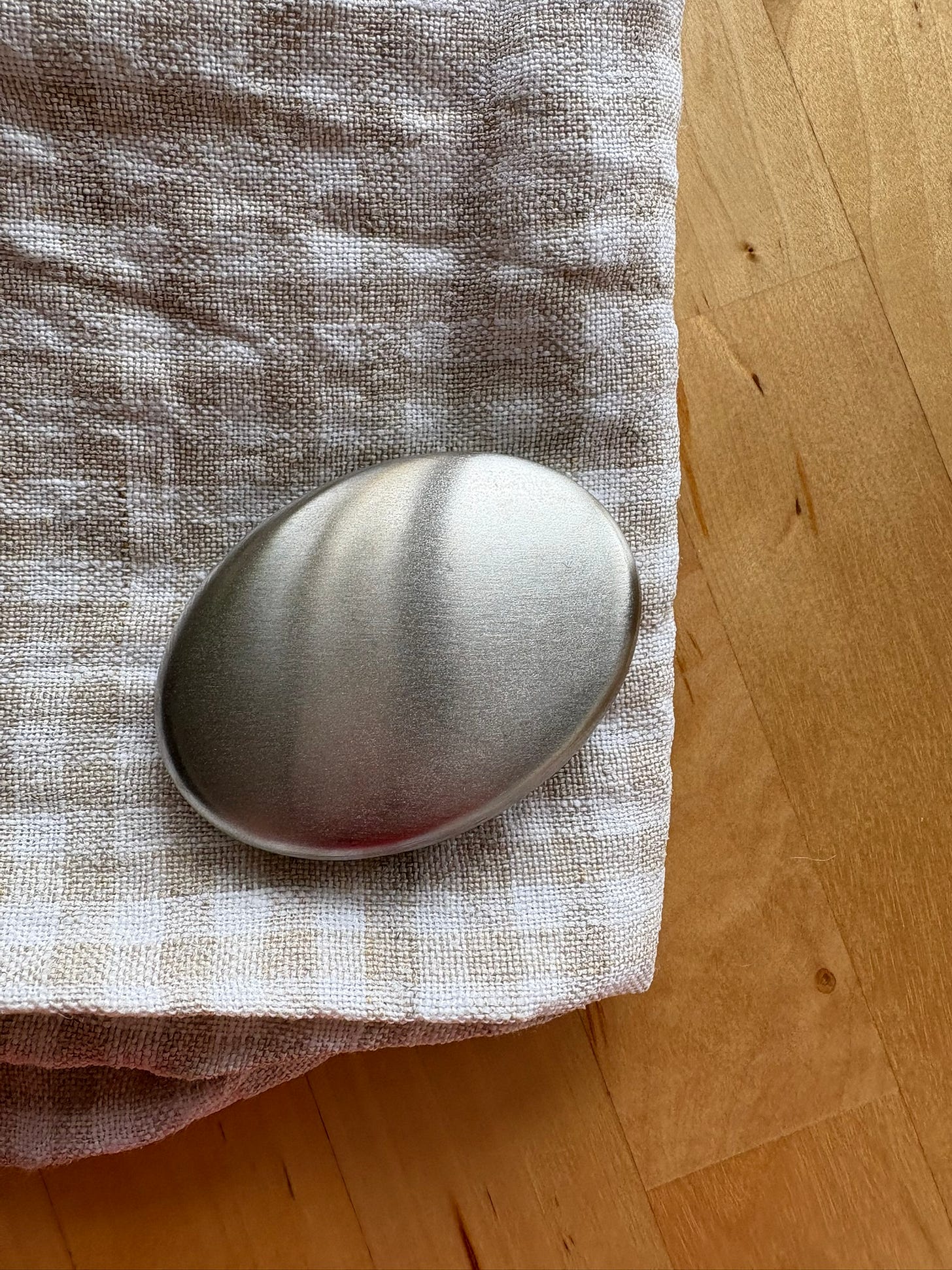 A stone-shaped piece of stainless steel on a white and taupe gingham linen tea towel that's resting on a wooden dining table.