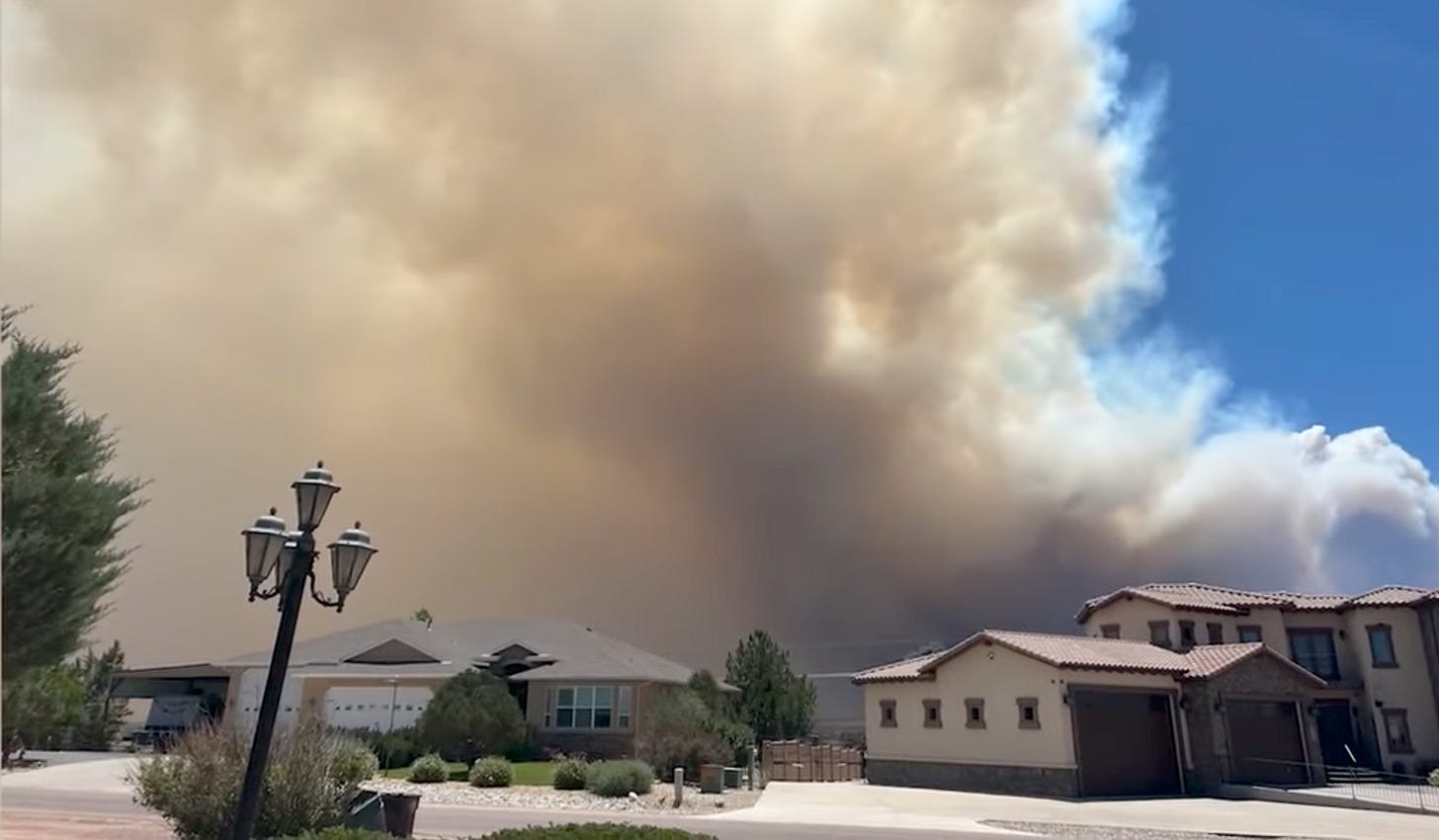 Thick smoke against blue sky towers over homes.