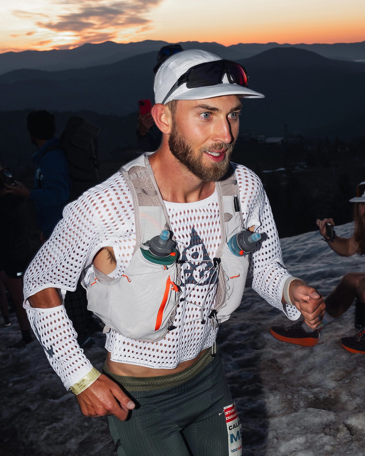 Man in a white cap, grey running vest, and the Nike Radical Airflow shirt running up a hill. 