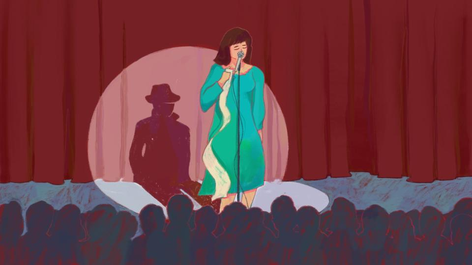 Woman on stage with a microphone and a piece of paper on her hand with her shadow as a stalker wearing a coat and a hat. 