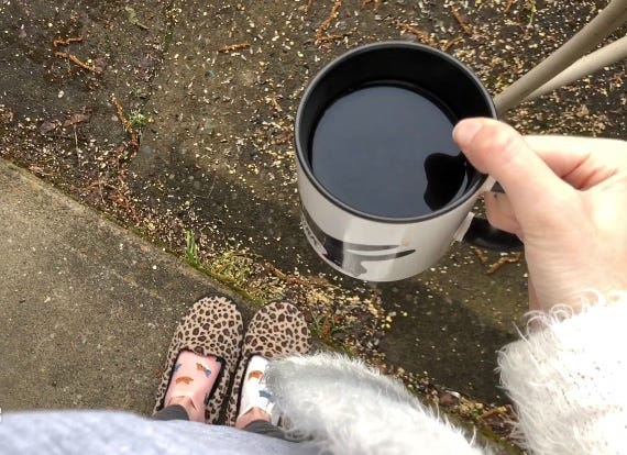 Outside: mug in woman's hand with feet showing beneath her—leopard print slippers and different colored socks.
